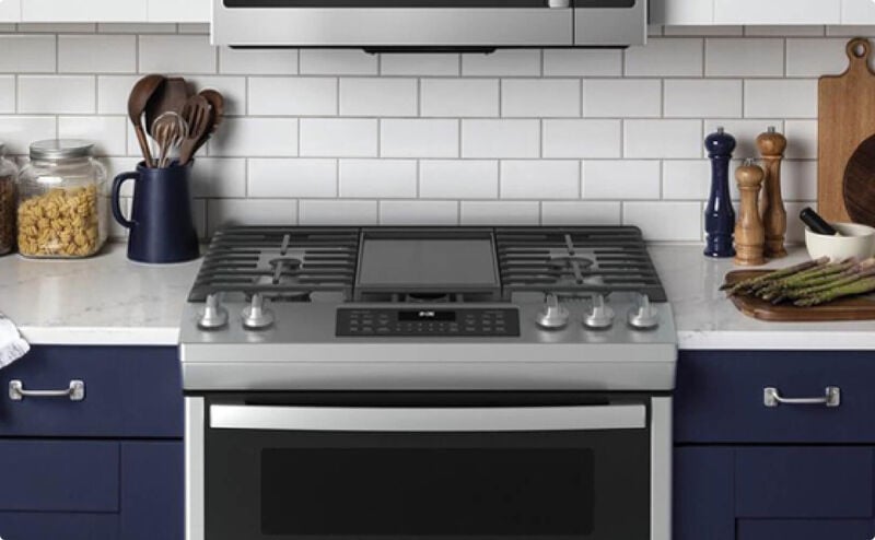 Stainless steel slide in range and microwave in a kitchen with navy cabinets and white granite countertops